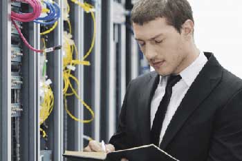 IT-Controller steht vor einem Server und macht sich Notizen