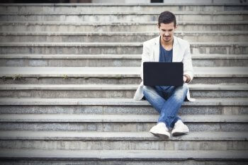 Junger Mann sitzt draußen mit Laptop auf Treppe